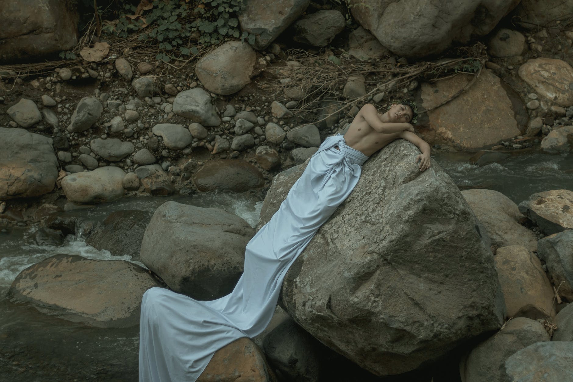 man lying on rocky stone near flowing water